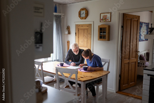 Female nurse helping senior man to solve sudoku in newspaper at home photo