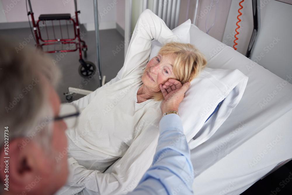 Elderly man touching female friend lying on bed in hospital Elderly man touching female friend lying on bed in hospital