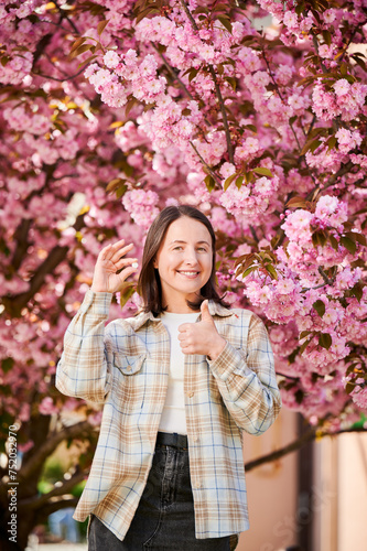 Woman allergic suffering from seasonal allergy at spring. Young happy woman showing allergy drugs, giving thumbs up, posing in blossoming garden at springtime. Antihistamine medication concept