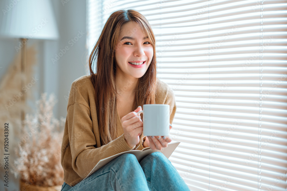 Joyful young asian female enjoying a cup of coffee while sitting on bench at home, Cosy scene, Smiling pretty woman drinking hot tea in autumn winter. Joyful young asian female enjoying a cup of coffee while sitting on bench at home, Cosy scene, Smiling pretty woman drinking hot tea in autumn winter.