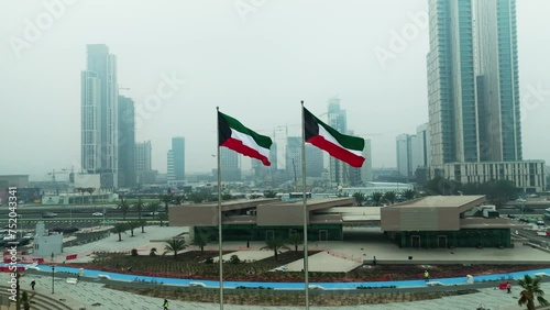 Kuwait flag waving in the sky with Kuwait buildings in the background photo