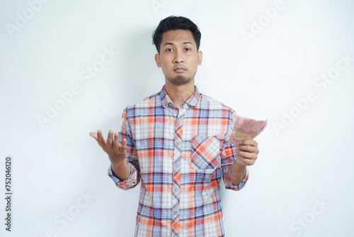 Adult Asian man holding money and looking camera with confused expression photo