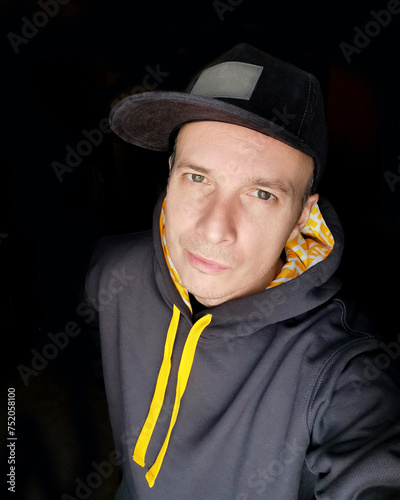 Selfie portrait on a smartphone, a man in a cap and hoodie on a black background