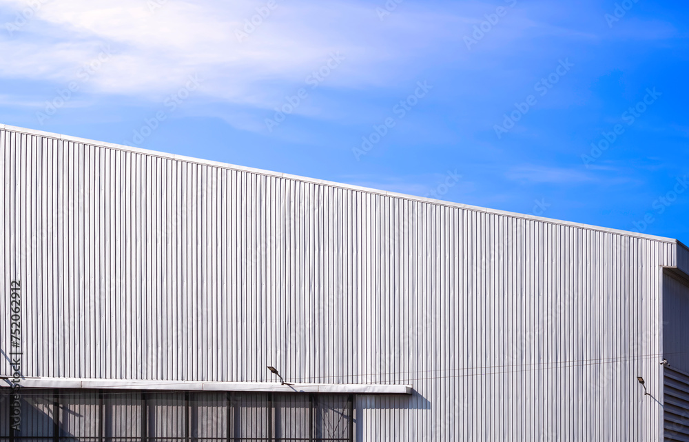 Aluminum corrugated industrial warehouse building and gable roof with sunlight reflection on metal wall surface against blue sky background