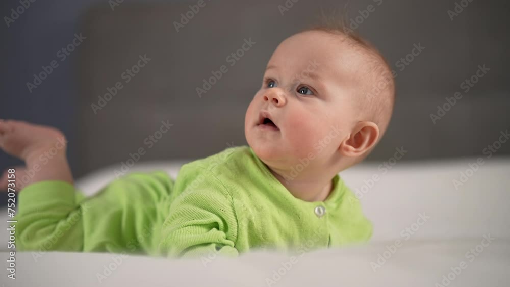 Portrait of little infant baby girl in yellow cotton bodysuit learning to hold head lying on stomach. Adorable little newborn relaxing alone on comfortable blanket at home. Shooting in slow motion. Portrait of little infant baby girl in yellow cotton bodysuit learning to hold head lying on stomach. Adorable little newborn relaxing alone on comfortable blanket at home. Shooting in slow motion.
