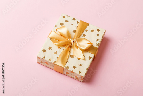 wrapped Christmas or other holiday handmade present in white paper with gold ribbon on colored background. Present box, decoration of gift on colored table, top view with copy space © sosiukin