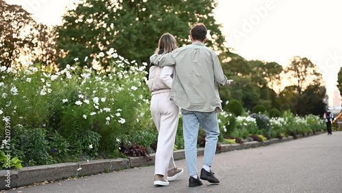 A young couple walks cutely through the park, view from the back