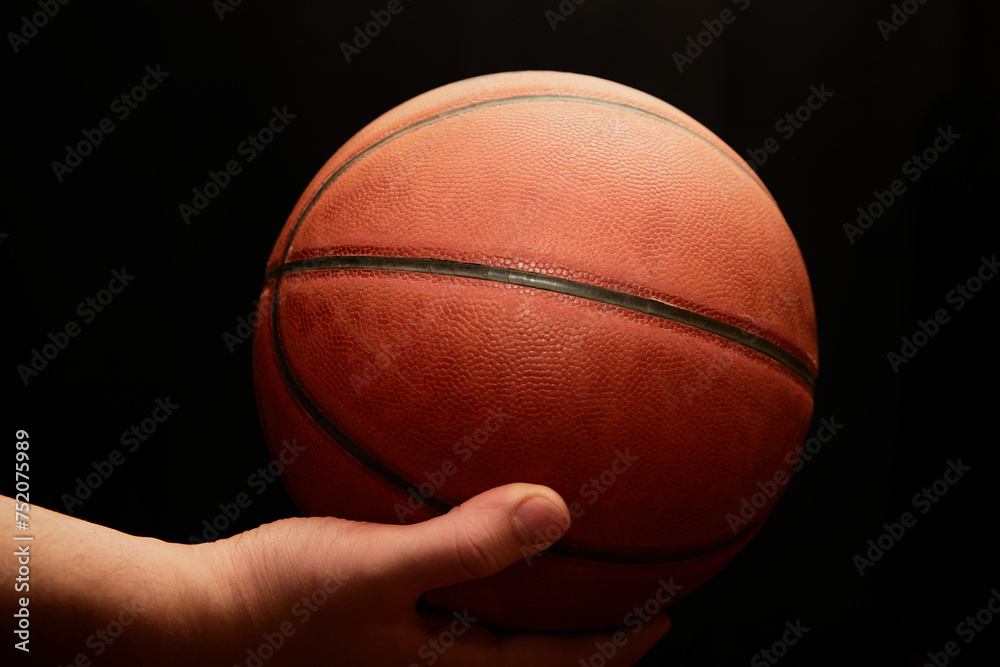 A hand holds a lit basketball on a black background, close-up, the start of the game, sports background