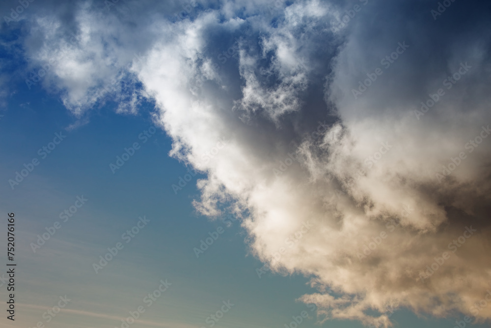 Obraz premium A large cumulonimbus rain cloud covers the blue sky, a large cloud in the sunlight on the blue sky.
