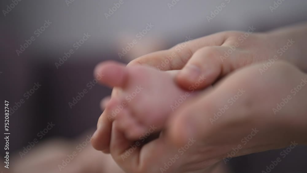 Close-up cropped shot of loving mother massaging newborn infant baby feet with thumbs tender touch parenting. Closeup of young mom touching legs of little infant kid lying on bed at home, slow motion. Close-up cropped shot of loving mother massaging newborn infant baby feet with thumbs tender touch parenting. Closeup of young mom touching legs of little infant kid lying on bed at home, slow motion.