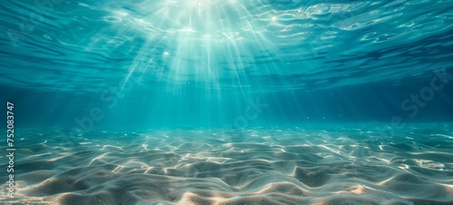 Underwater view of a sandy seabed with clear blue tropical water above, illuminated by sunlight filtering through the surface. The image evokes a serene, pristine ocean environment. © Maxim