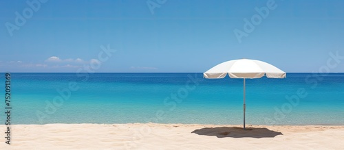 Tranquil Beach Scene with a White Umbrella Providing Serene Shade Against a Deep Blue Ocean © vxnaghiyev