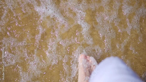 Feet stepping into sea foam as waves recede on a sandy beach in 4k slow motion 120fps