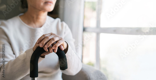 Billede på lærred An elderly woman holding a walking stick sat alone and sad looking out the window