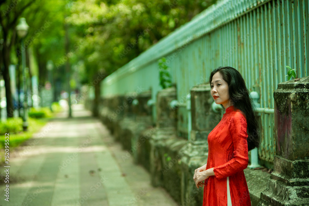 Woman wearing traditional Vietnamese ao dai walking on the road of flying tamarind leaves