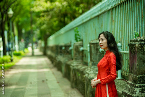 Woman wearing traditional Vietnamese ao dai walking on the road of flying tamarind leaves