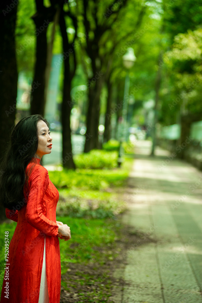 Woman wearing traditional Vietnamese ao dai walking on the road of flying tamarind leaves.Portrait of woman wearing black sunglasses while standing behind friend. Woman wearing traditional Vietnamese ao dai walking on the road of flying tamarind leaves.Portrait of woman wearing black sunglasses while standing behind friend.