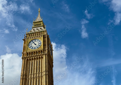 A low angle view of Big Ben against a blue sky with light clouds in Westminster, London, UK.  photo