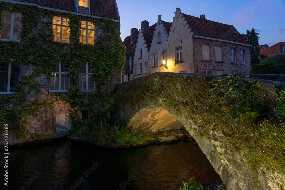 Peerden bridge and historic buildings reflected on the canal in the old town of the beautiful city of Brugge in Belgium at night.