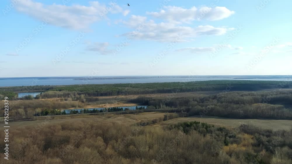 Aerial view, moving slowly forward, in late autumn, showing leafless trees, Lake of Two Mountains and a bird flying in the blue sky.