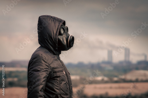 man in a gas mask and a hood amid smoke from factory pipes