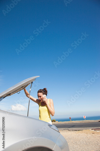 Woman Looking under Car Hood whilst Talking on the Phone
