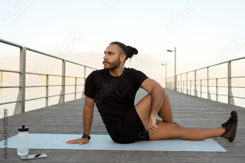 young man in activewear performing seated spinal twist asana outdoor