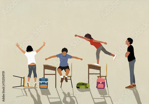 Frustrated teacher watching hyper schoolchildren jumping on desks in classroom
 photo