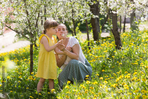 mom and little daughter  embrace and blow on a dandelion in a flowering garden in spring..  stress relief. Spring awakening. Slow life. Enjoying the little things. Dreaming of spring. 