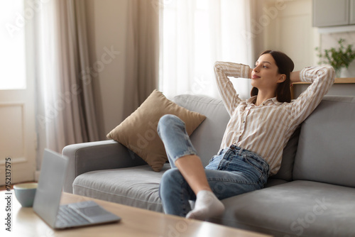 Wall Mural Relaxed young woman lounging on sofa in front of laptop on table