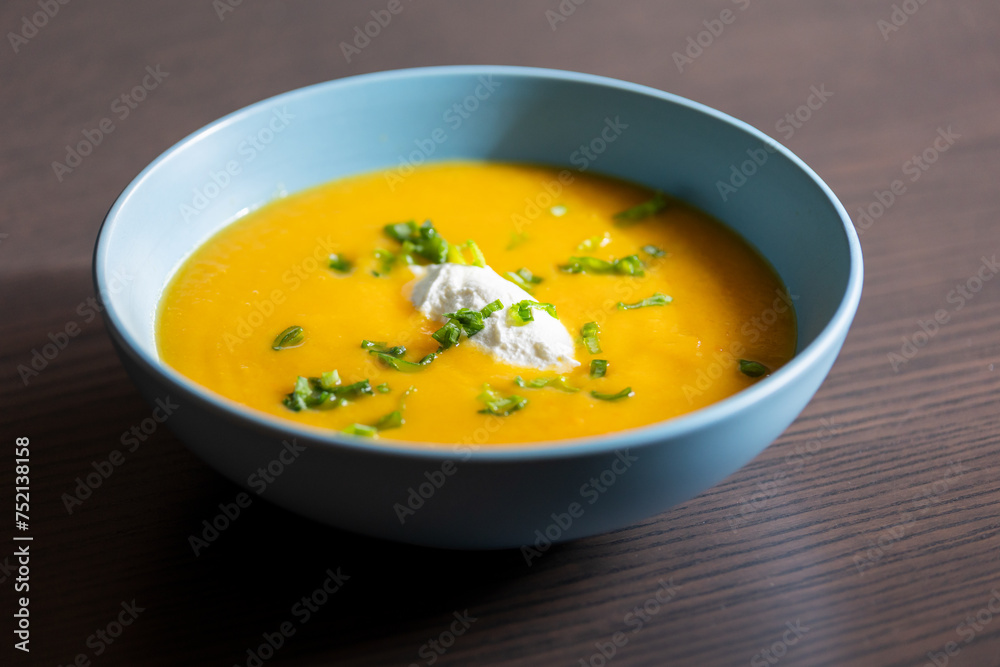 delicious carrot soup in a bowl with cream and green onion close-up delicious carrot soup in a bowl with cream and green onion close-up
