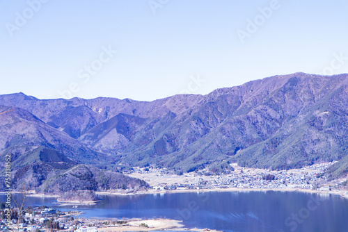Landscape Forest Lake with mountain blue sky and bright sunlight in background. Hills, lagoon of smoky mountain range covered in white mist and deciduous forest. Dry forests in winter or autumn.