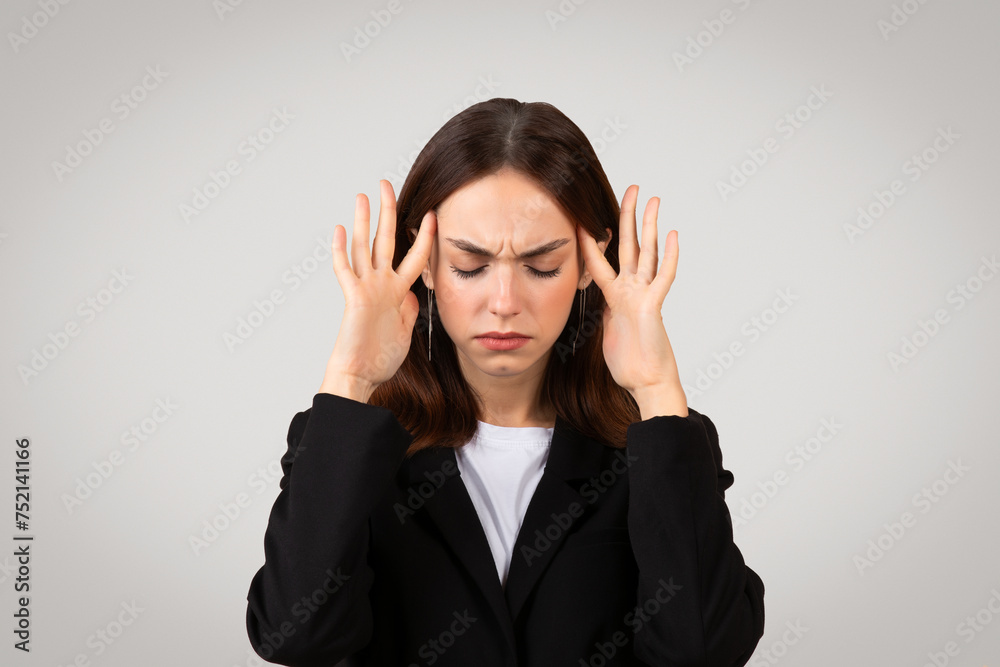 Stressed young businesswoman with a pained expression holds her temples Stressed young businesswoman with a pained expression holds her temples