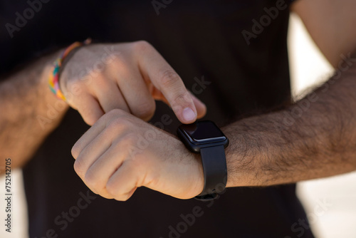 Unrecognizable man in fitwear uses smartwatch for workout monitoring outdoors