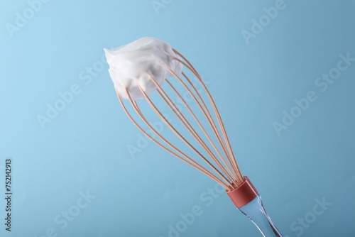 Whisk with whipped cream on light blue background