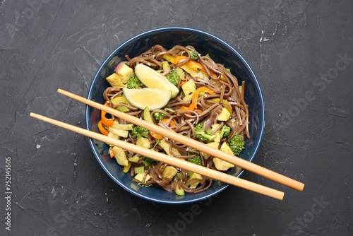 Stir-fry. Delicious cooked noodles with chicken and vegetables in bowl served on gray textured table, top view