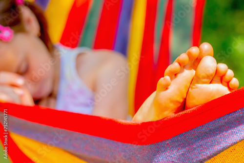 Young beautiful girl sleeping in a hammock with bare feet, relaxing and enjoying a lovely sunny summer day. Safety and happy childhood and leisure concept. Selective focus