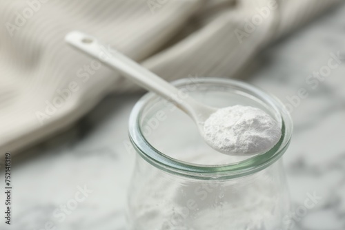 Baking powder in jar and spoon on white table, closeup. Space for text