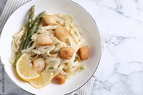 Delicious scallop pasta with asparagus and lemon on white marble table, top view. Space for text