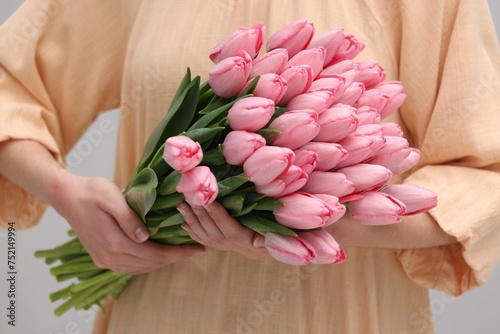 Woman holding bouquet of pink tulips on light grey background, closeup