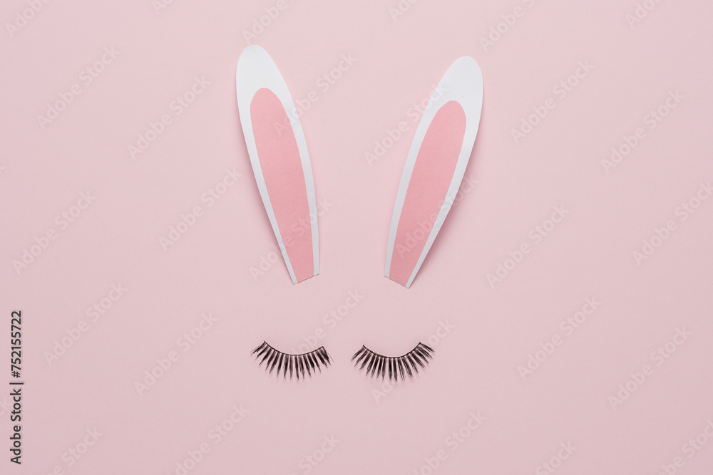 Minimal Easter concept. Bunny rabbit face made of paper bunny ears with eyelashes on pastel pink background. Flat lay.