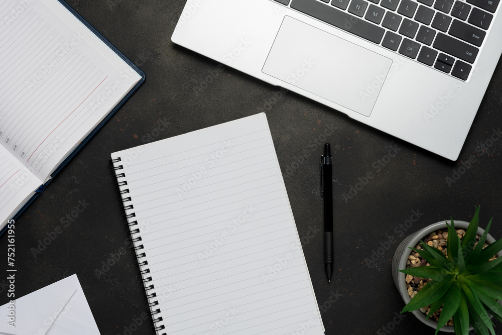 Workspace with blank notebook, laptop, office supplies and green leaves on black background. Workspace with blank notebook, laptop, office supplies and green leaves on black background.