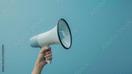 Hand holding a megaphone against a clear blue sky, symbolizing communication power.