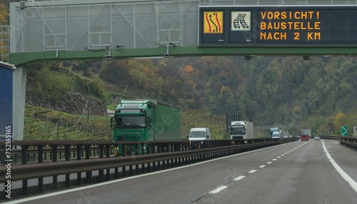 Cars and trucks traffic on the Brenner motorway at an upcoming construction site. A sign lights up above the road: “Caution: construction site after 2 km”