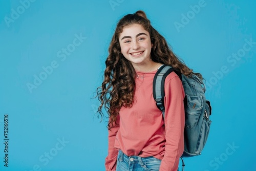 Teen fashion model smiles at the camera, dressed in contemporary casual wear with a backpack, set against a blue background with advert space. Generated AI