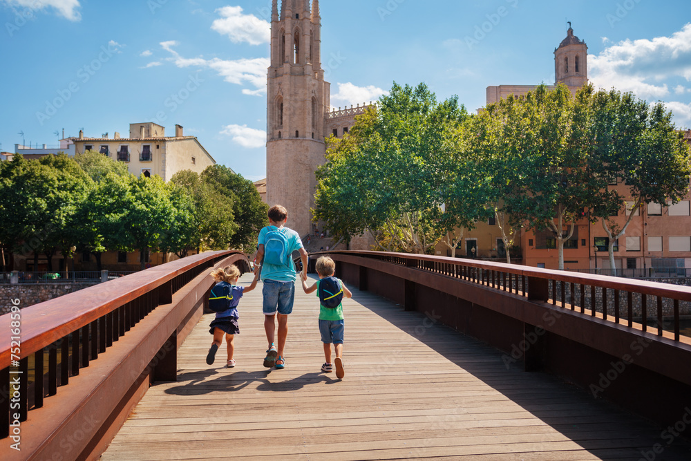 Children travelers with backpacks cross the bridge in Girona