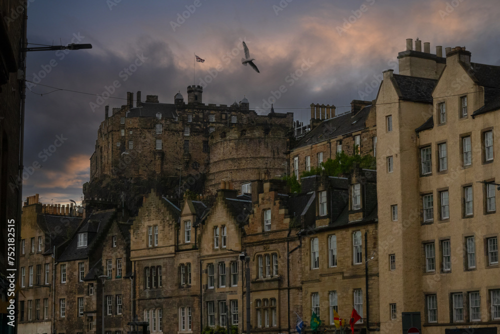 Famous Edinburgh Castle above rooftops of old stone townhouses on a cloudy day
