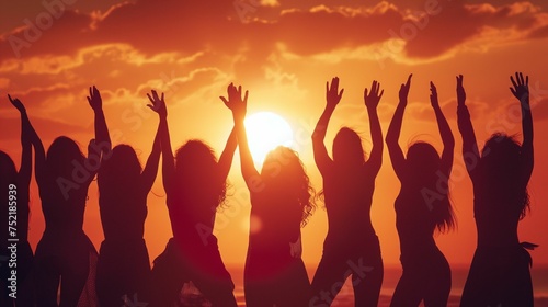 Silhouettes of many women with their hands raised in the background of the sunset.