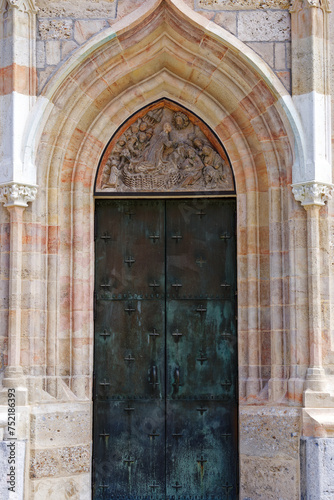 Old town of Kranj with entrance of church named St. Kancijan’s Church with bronze gate and stone sculptures on a sunny summer day. Photo taken August 10th, 2023, Kranj, Slovenia. © Michael Derrer Fuchs