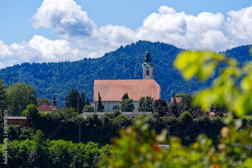 Beautiful view with church and woodland and mountain panorama in the background at Slovenian City of Kranj on a sunny summer day. Photo taken August 10th, 2023, Kranj, Slovenia.